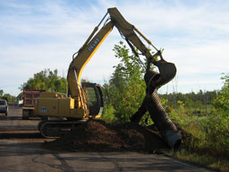 Kadlec Excavating backhoe pulls rusted culvert out of soil.
